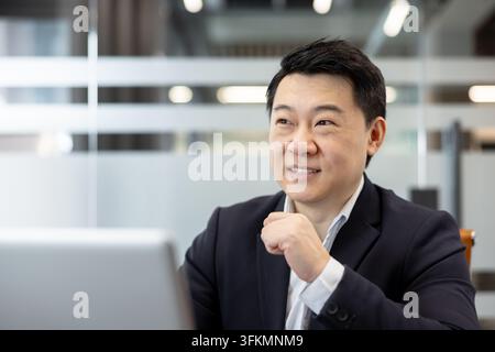 Businessman working on laptop in modern office, professional man looking at screen with focus. Corporate employee engaged in financial analysis and digital communication at desk during work. Stock Photo