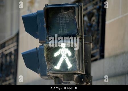 A glowing white walk signal on a weathered pedestrian traffic light covered in spider webs, photographed in Buenos Aires, Argentina. Stock Photo