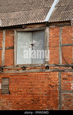 Old red brick building facade with weathered wooden beams and metal shutters Stock Photo