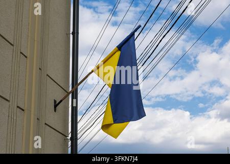 Ukrainian Flag Hanging on Building Against Blue Sky with Clouds Stock Photo