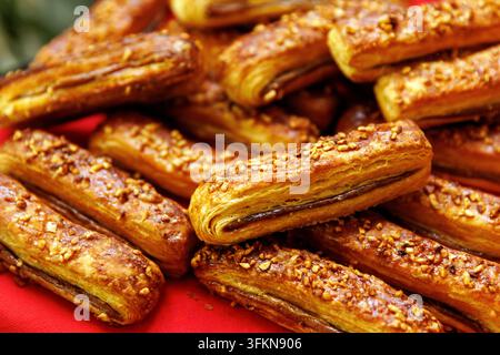 Macro shot of baked puff pastry finger sticks topped with chopped nuts and filled with sweet chocolate filling served on red cloth. Stock Photo