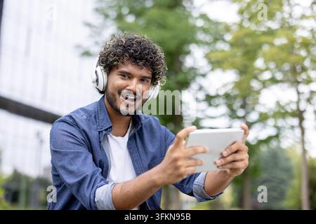 Happy student using a tablet for online education on a university campus. Young man studying with headphones and a digital device for academic research and e learning course preparation. Stock Photo