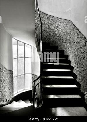 Elegant curved staircase with marble steps and mosaic tile walls in 1950s Rationalist style building in Pescara, Italy Stock Photo