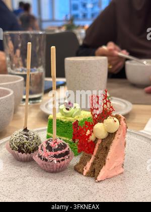 A variety of gourmet miniature desserts including chocolate cake pops, a green layered cake, and a frosted cake slice served in a cafe setting. Stock Photo