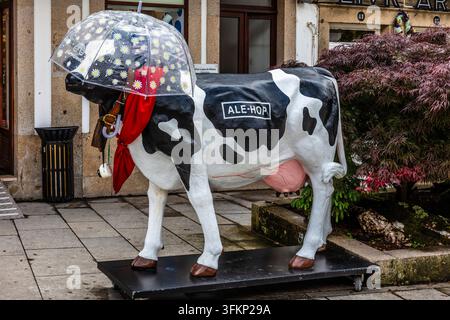 Famous black and white plastic cow from the Spanish gift chain Ale-Hop standing in front of a branch with an umbrella and a red cloth, Ponte de Lima, Stock Photo