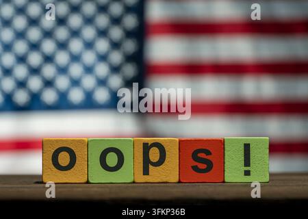 Oops word on blocks and US flag background, close up. The word oops written on colorful wooden toy blocks in front of blurred American flag background Stock Photo