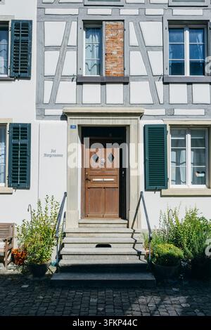 Historic entrance of a traditional half-timbered house with a brown, decorated wooden door, a small stone staircase in front and dark green shutters o Stock Photo