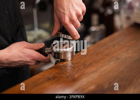 A barista pressing ground coffee with a metal tamper into a portafilter Stock Photo
