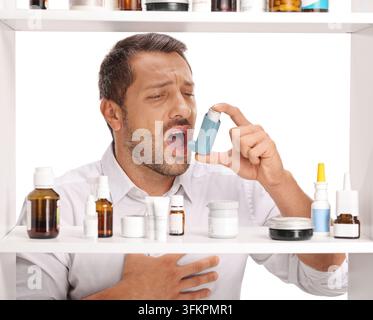 Man using an asthma inhaler in front of a medicine cabinet Stock Photo