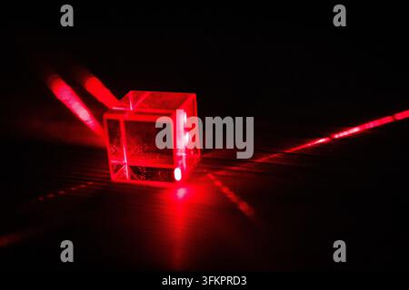 A close cube shines with internal red light while outgoing beams sketch crisp lines across the bench capturing refraction and reflection in a compelli Stock Photo