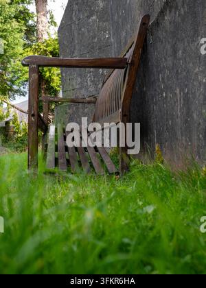 20th September 2026, Loweswater, United Kingdom. An old wooden bench rests against a weathered concrete wall, surrounded by lush green grass and trees Stock Photo