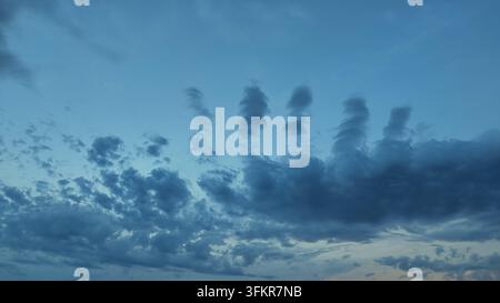 Unusual cloud formations creating vertical shapes against a light blue sky Stock Photo