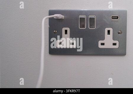 UK Wall Socket with USB Charging Ports - A close-up view of a modern brushed metal UK double power socket featuring two integrated USB charging ports Stock Photo