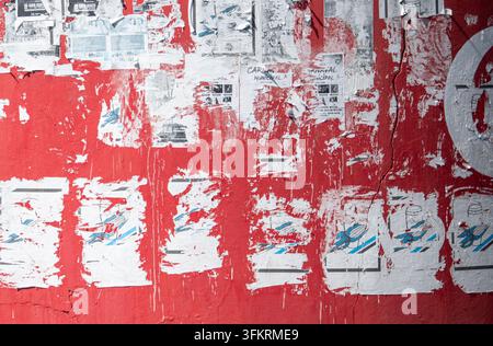A textured street scene featuring layers of white paper posters that have been torn, peeled, and scratched off a vibrant red painted wall, creating a Stock Photo