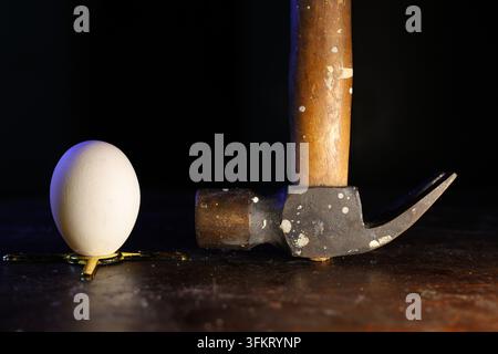 Fragility and Strength. Conceptual low-key still-life of a fresh egg placed next to a vintage claw hammer on a dark background. Stock Photo