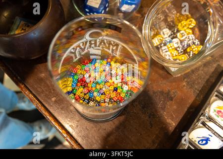 Close-up view of colorful dice with visible pips resting in clear glass cups on rustic wooden tabletop with warm indoor lighting, game day mood in Bos Stock Photo