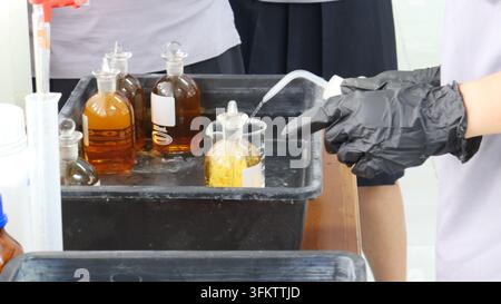 Student wearing black gloves cleaning laboratory glassware with a wash bottle Stock Photo