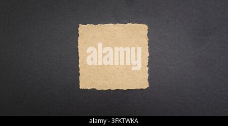 torn beige paper square centered on a dark textured background, suitable for message, note, copy space, and handmade design concepts. Stock Photo