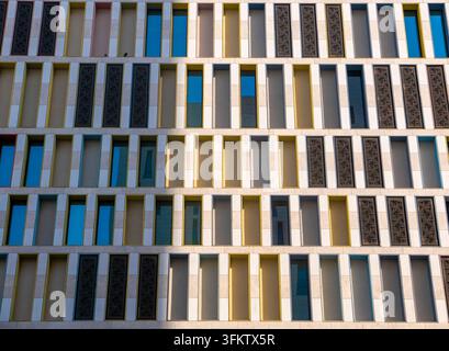 Modern building exterior facade featuring a colorful grid of vertical rectangular windows and ornate decorative pattern panels in daylight. Stock Photo