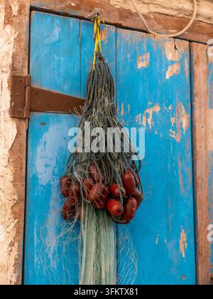 Traditional fishing net with red floats hanging on a weathered blue wooden door beside a textured wall in Souq Waqif. Stock Photo