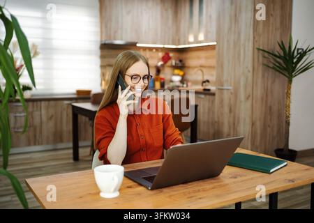 Woman multitasking working remotely from home on laptop and phone Stock Photo