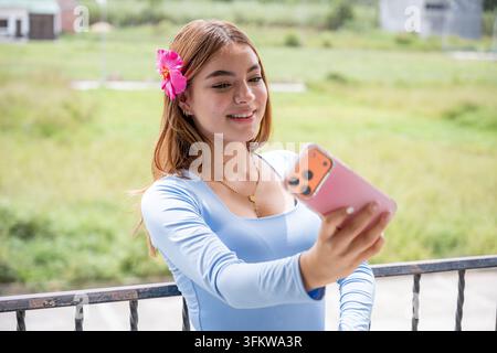 Young woman taking a selfie outdoors, smiling while holding her smartphone, actively engaging with social media and digital content, representing yout Stock Photo