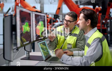 Automotive Engineer Carefully Inspects Electric Car Assembly Line Using Laptop. Stock Photo