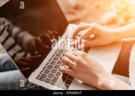 Typing laptop hands woman working on portable computer outdoors during golden hour in casual clothing with warm sunlight Stock Photo