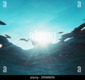 Crystal clear ocean water illuminated by bright tropical sunlight creating glowing rays and floating particles below surface Stock Photo