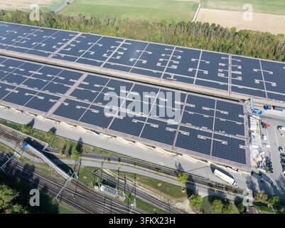 Aerial view of the Decathlon Switzerland logistics center featuring a large-scale solar panel array on its roof, near railway tracks and green landsca Stock Photo