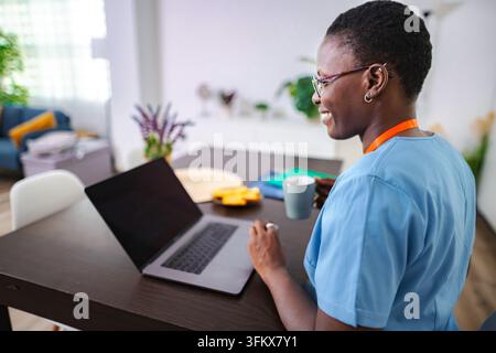 Black woman nurse working on laptop at home Stock Photo