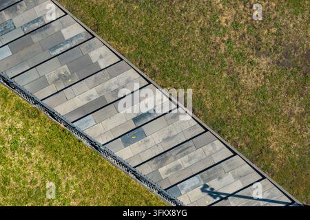 Aerial view of a stone-paved path with a metal railing running through a green grassy area in Poland. Stock Photo