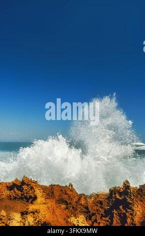 Powerful ocean wave collides violently with rugged coastline, framed by endless, clear sky above Stock Photo