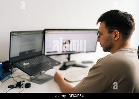 Over shoulder view of male professional working on computer with dual screen setup. Man in glasses focuses on task. Bright, modern workspace illustrat Stock Photo