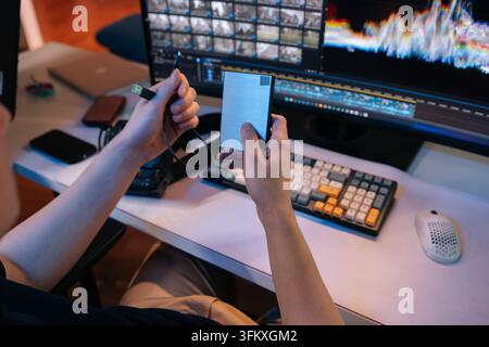 Creative professional holding and connecting external hard drive to computer, ensuring data storage and backup during demanding video editing process Stock Photo