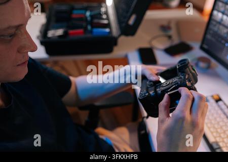 Photographer at workstation inserting memory card into professional digital camera, preparing for shoot or transferring data for post production editi Stock Photo