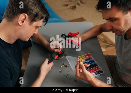 High angle view of two technicians collaborating on wiring job. Hands holding tools and colorful connectors from plastic organizer box. Teamwork and D Stock Photo