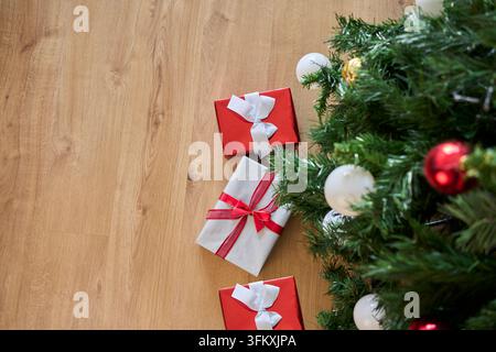 Beautifully wrapped Christmas gifts and  Christmas crackers placed beside a Christmas tree. Christmas background with decorations and gift boxes on wo Stock Photo