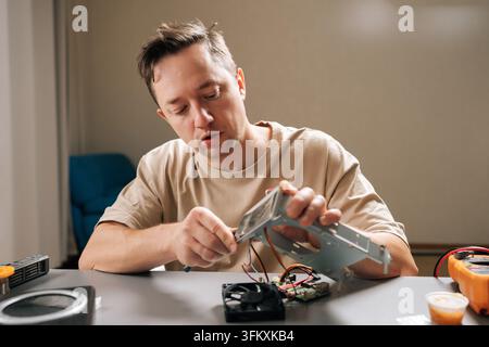 Focused young adult repairman fixing computer hardware components, examining circuit boards and connecting wires to diagnose issues and perform mainte Stock Photo