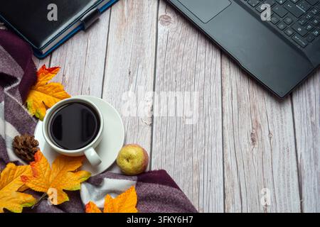 Coffee cup, laptop, and fall leaves on wooden desk Stock Photo