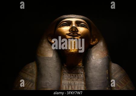 COPENAGHEN, DENMARK - AUGUST 25 2025: Close-up of a gilded ancient Egyptian anthropoid sarcophagus lid face with nemes headdress on dark background. Stock Photo