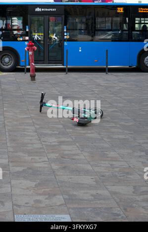 Budapest, Hungary - September 21, 2026: An abandoned electric scooter lying on the paved street next to a red fire hydrant and a blue public bus. Stock Photo
