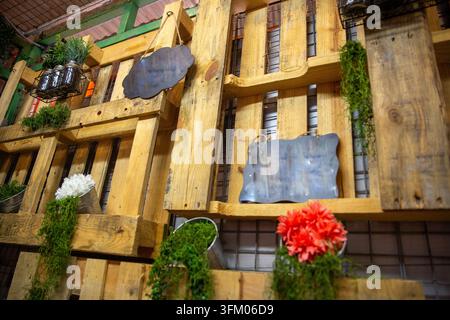An angled, close-up photograph showcasing a rustic accent wall built from recycled wooden pallets, decorated with hanging chalkboards, metal flower bu Stock Photo