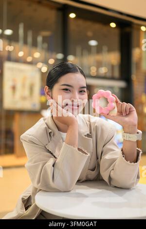A charming vertical portrait of a smiling young Southeast Asian Thai woman from the Isan region sitting at a table in a shopping mall cafe while holdi Stock Photo
