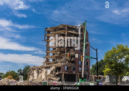 A high-reach demolition excavator with a water sprayer works on a multistory building undergoing demolition on "Fairfax Dr." Stock Photo