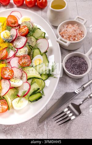 Fresh colorful salad with sliced tomatoes, cucumber, radishes, yellow bell pepper and quail eggs, with dill, olive oil and Himalayas and black salt on Stock Photo