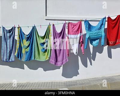 Colorful laundry hanging on a clothesline against a white wall with shadows Stock Photo
