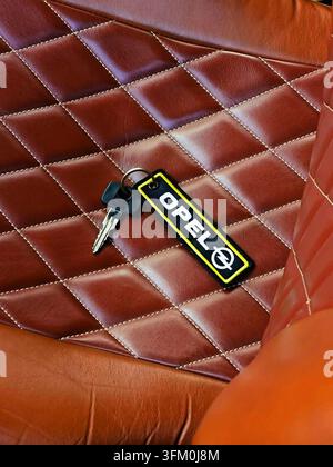 Key with Opel keychain resting on a luxurious brown leather quilted car seat Stock Photo