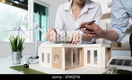 A woman and a man working on a model of a house. The woman holds a pen and the man is holding a ruler. Scene is focused and determined how they work t Stock Photo