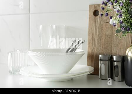 White bowls and plates with flowers and kitchen accessories in clean modern kitchen interior Stock Photo
